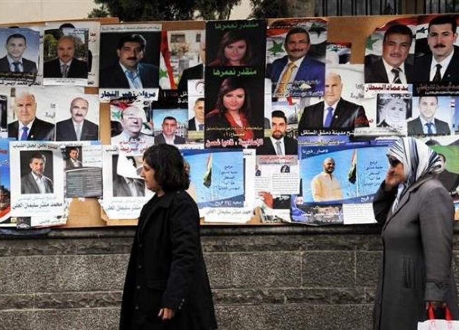 Two Syrian women walk by the posters of candidates for Syria