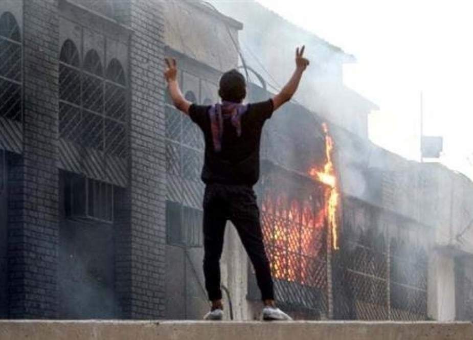 An Iraqi protester stands on the ledge of a wall watching the burning of the Basra airport