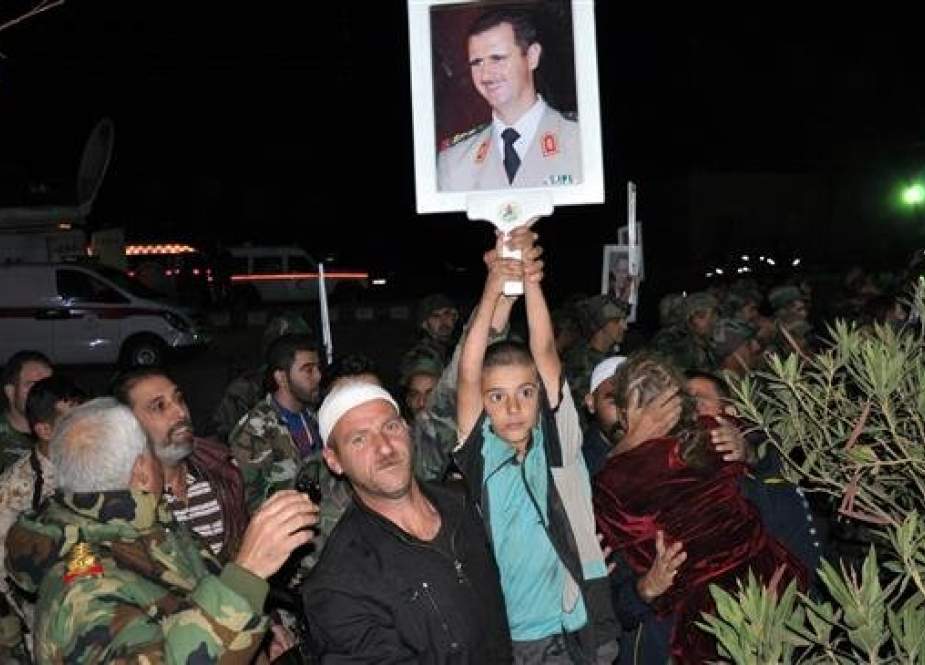 This handout picture released by SANA on November 9, 2018 shows a boy holding up a picture of Syrian President Bashar al-Assad as a group of recently-freed hostages, abducted in July from Suwayda by Daesh, are being welcomed by relatives upon their arrival overnight in their hometown in the southern Syrian province of Suwayda. (Via AFP)