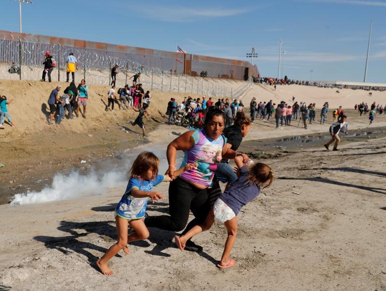 A migrant family, part of a caravan of thousands traveling from Central America en route to the United States, runs away from tear gas in front of the border wall between the U.S and Mexico in Tijuana, Mexico November 25, 2018.