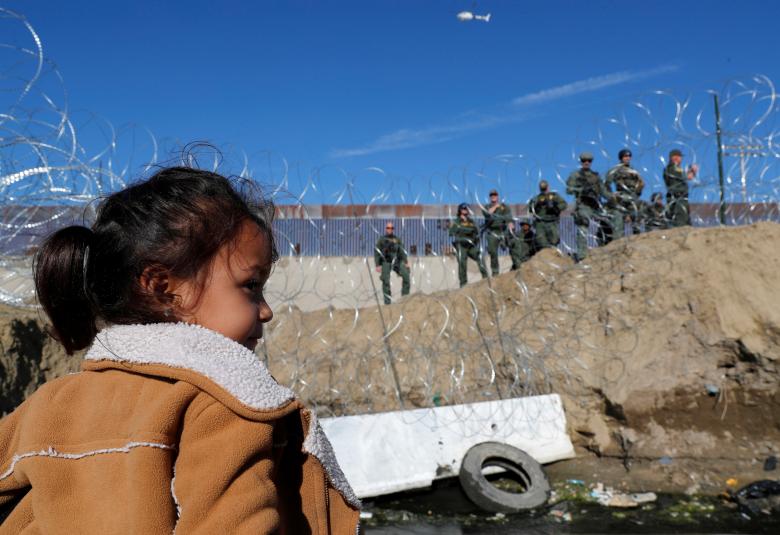 A migrant girl stands in front of the border fence between Mexico and the United States in Tijuana, Mexico, November 25, 2018.