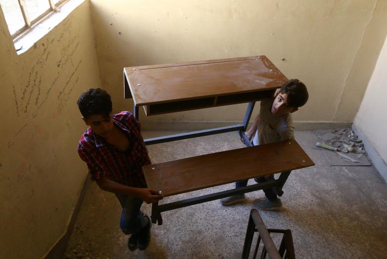 School children hold a desk in Raqqa, Syria September 17, 2018. Islamic State used Raqqa s schools - like much of the city - for military purposes, digging tunnels under some of them. Some of the schools were hit by air strikes, Raqqa residents say.