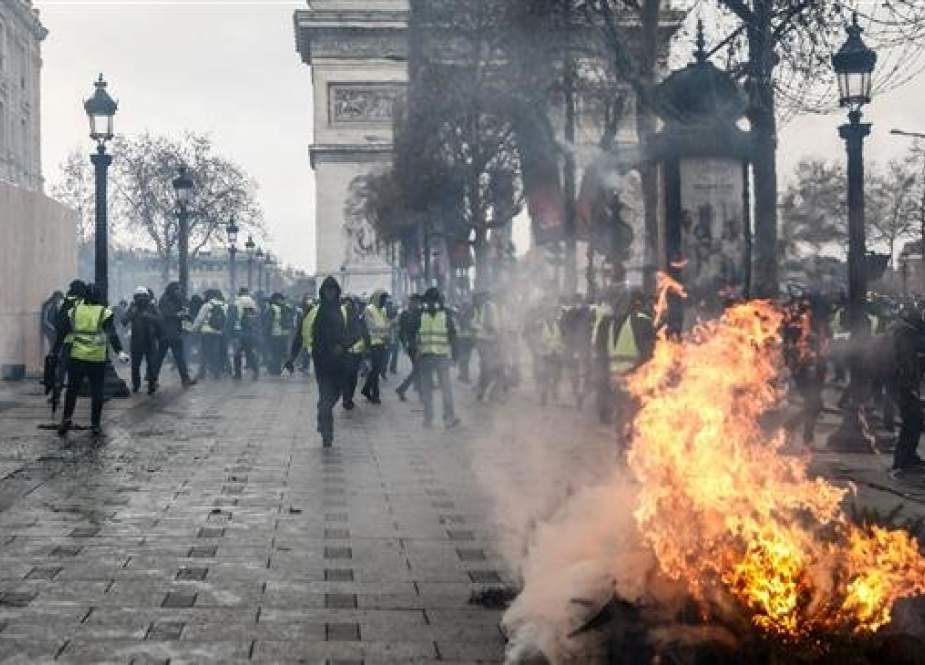 Protesters wearing yellow vests (gilets jaunes) stand next to a burning tree, as they demonstrate against rising costs of living they blame on high taxes near the Arc de Triomphe on the Champs-Elysees avenue in Paris, on December 8, 2018. (AFP)