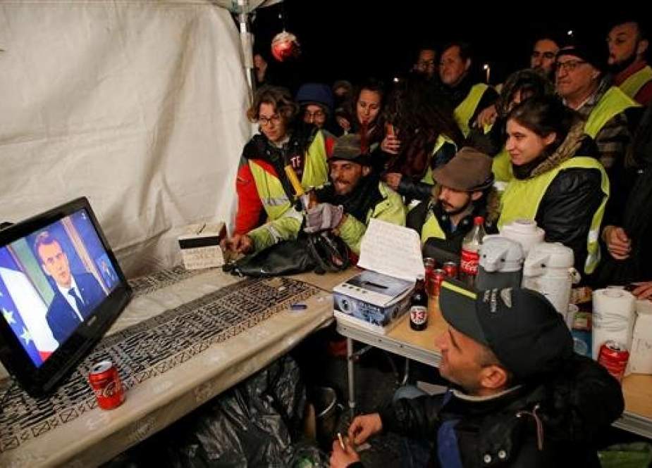 French protesters wearing yellow vests watch French President Emmanuel Macron on a TV screen at the motorway toll booth in La Ciotat, near Marseille, France, on December 10, 2018. (Photo by Reuters)