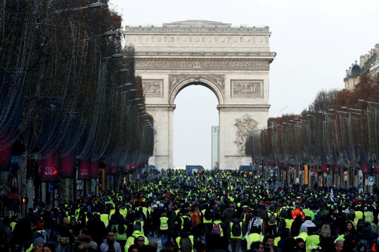 Protesters wearing yellow vests walk on the Champs-Elysees Avenue with the Arc de Triomphe in the background during a national day of protest by the 