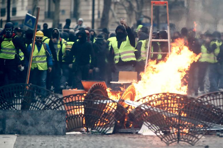 Protesters wearing yellow vests stand behind a barricade as they face off with police during clashes as part of a national day of protest by the 