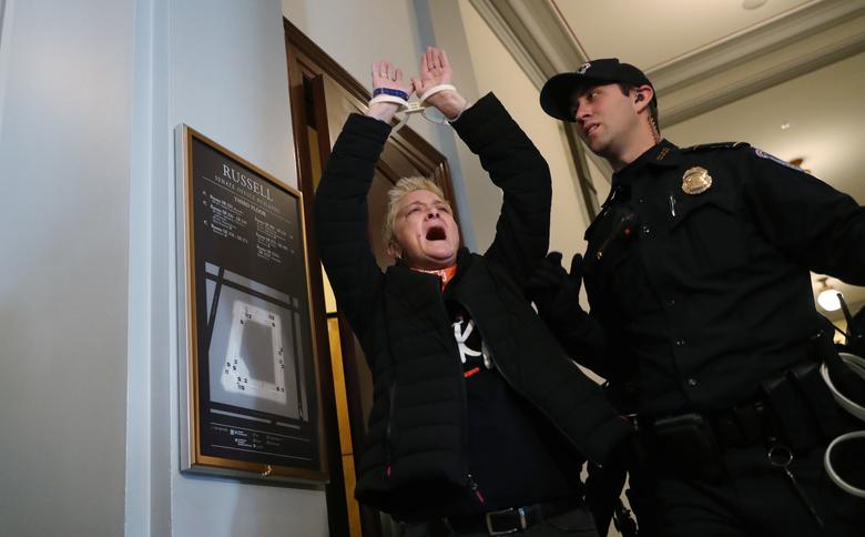 A protestor detained outside Senate Majority Leader Mitch McConnell's office is led away by a Capitol police officer during a demonstration against the partial government shutdown on day 33 in the Russell Senate office building on Capitol Hill in Washing