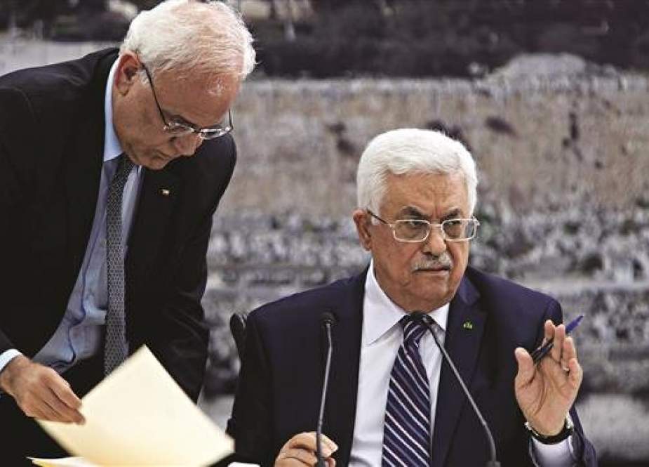 In this file photo Palestinian chief negotiator Saeb Erekat (L) helps Palestinian President Mahmoud Abbas as he signs international conventions during a meeting with Palestinian leadership in the occupied West Bank City of Ramallah on April 1, 2014. (Photo by Reuters)