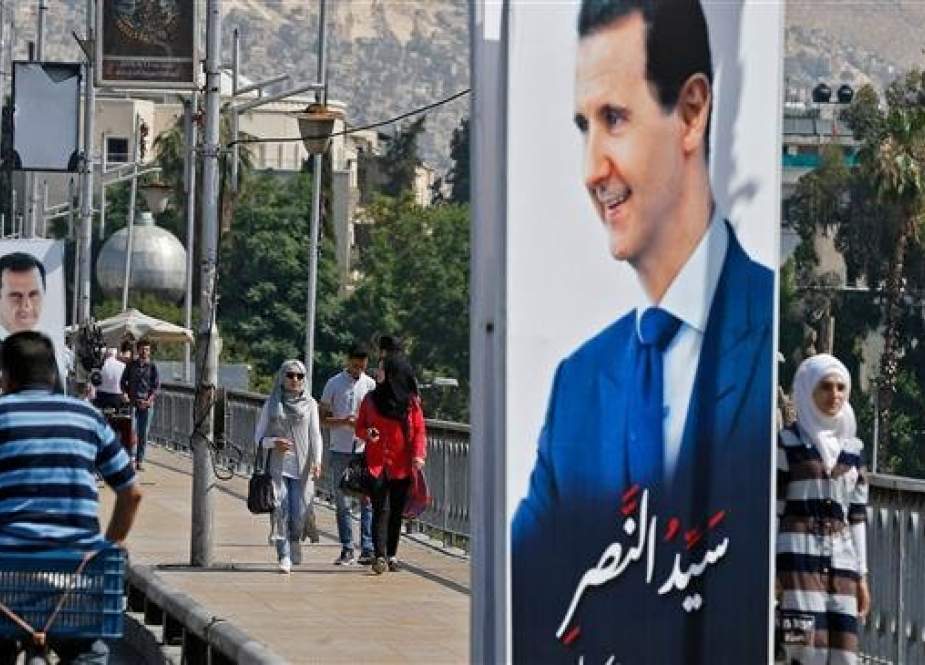 People walk near a portrait of Syrian President Bashar al-Assad hanging in a street in the Syrian capital Damascus on May 31, 2018. (Photo by AFP)