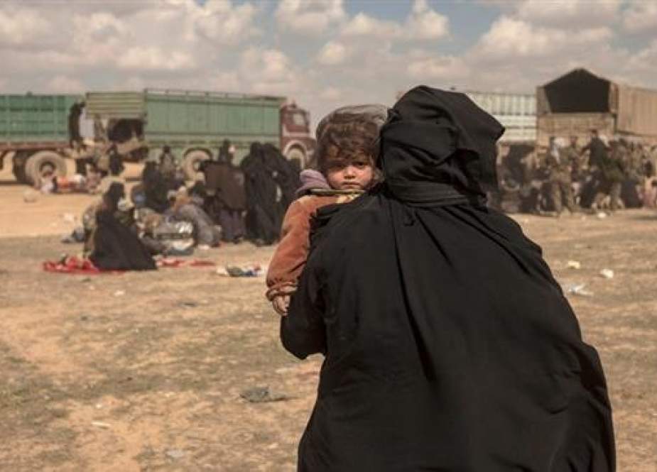 The picture taken Ion March 6, 2019 shows a woman carrying her child at a reception area for people evacuated from the last shred of territory held by Daesh terrorists, outside Baghouz, Syria. (By AP)