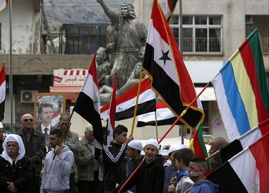 Druze demonstrators in the Golan Heights wave Syrian and Druze flags as they gather in front of a portrait of Syrian President Bashar Assad during a protest against US President Donald Trump, in the town of Majdal Shams, on March 23, 2019. (Photo by AFP)