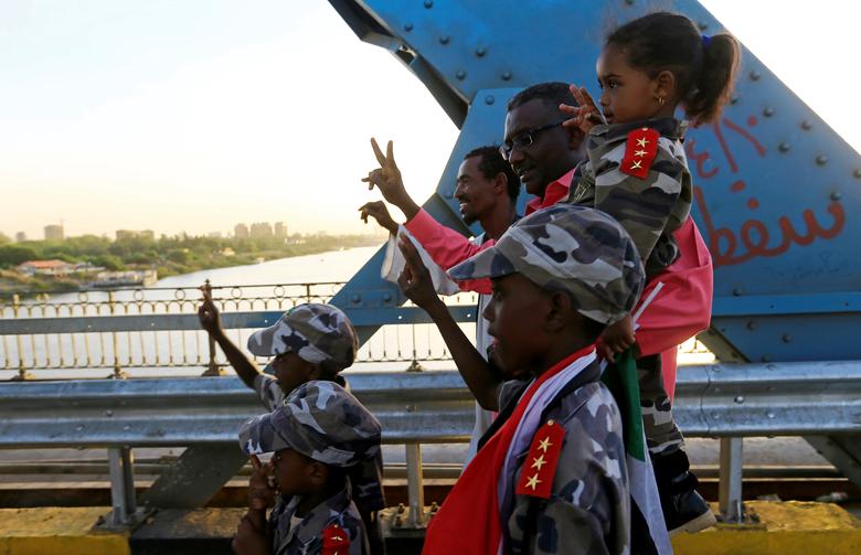 Members of a Sudanese family flash the victory sign as they walk on a railway bridge during a sit-in protest outside the Defence Ministry in Khartoum, April 15