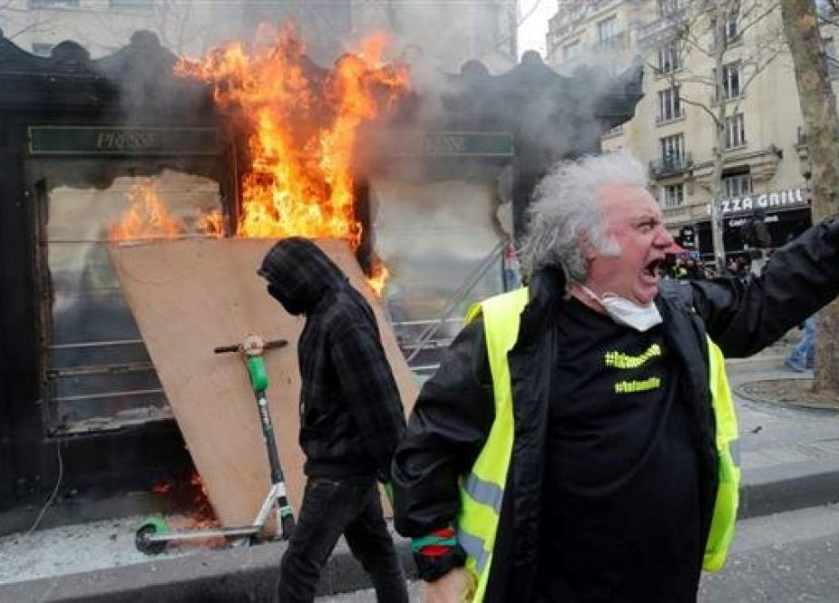 A yellow vest protester gestures in front of a newsagent set alight during clashes with riot police forces on the Champs-Elysees in Paris on March 16, 2019. (Photo by AFP)