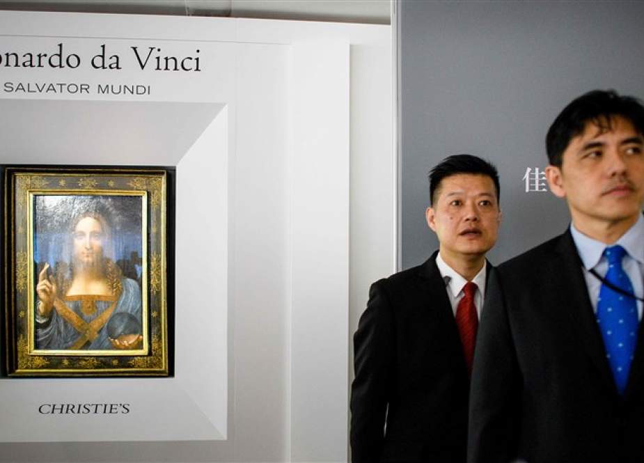 This AFP picture taken on October 13, 2017, shows a man (R, wearing blue tie) identified by local Hong Kong media as former CIA agent Jerry Chun Shing Lee standing in front of a member of security at the unveiling of Leonardo da Vinci