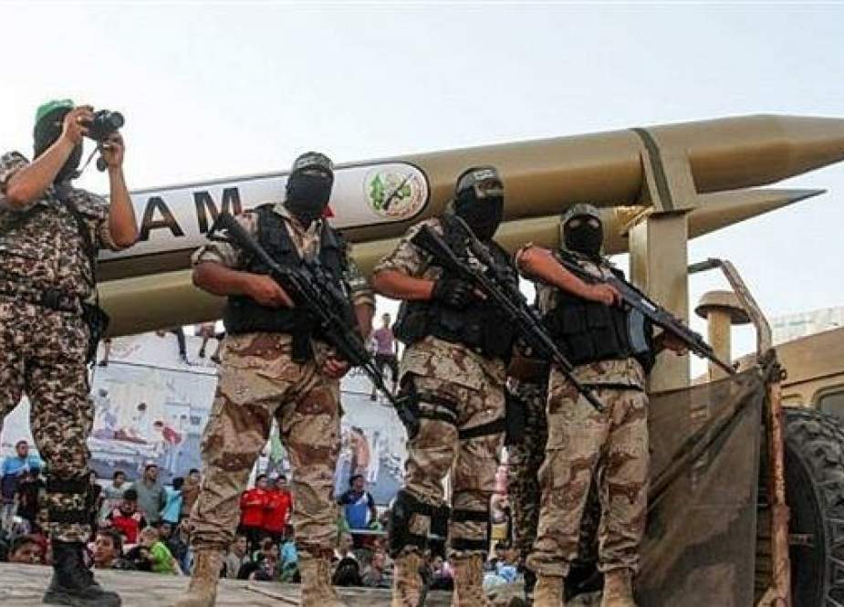 Armed Palestinian resistance fighters stand on a platform truck carrying two variants of Qassam short-range missiles.