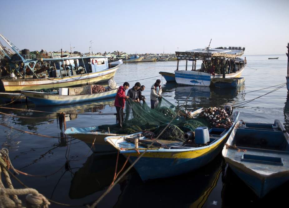 Palestinian fishermen sit in a beached fishing boat as they repair a fishing net along the coast in Khan Yunis in the southern Gaza Strip.
