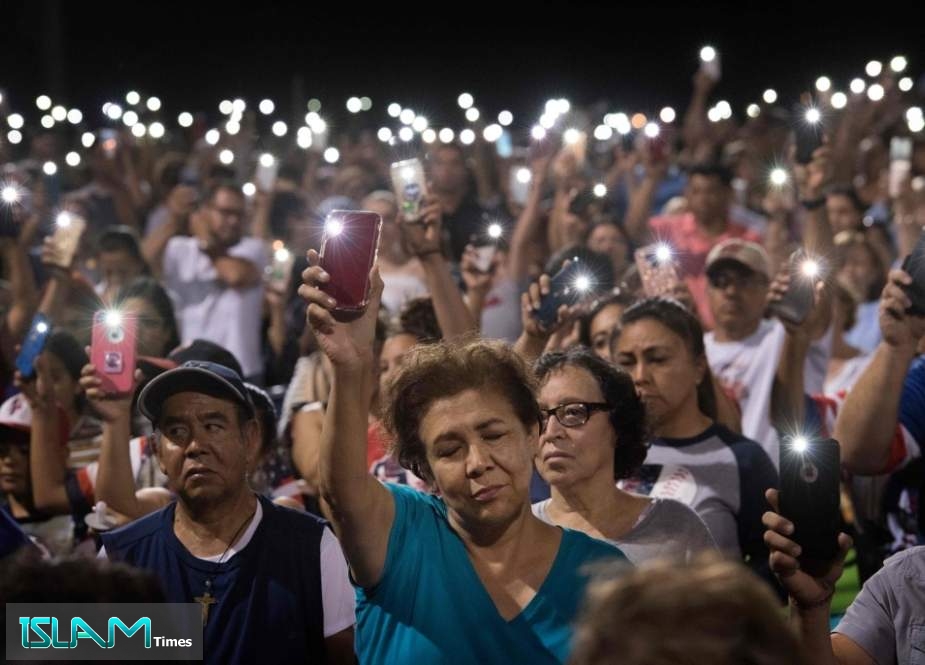 People hold up their phones during a prayer and candle vigil organized by the city, after a shooting left 20 people dead at the Cielo Vista Mall Wal-Mart in El Paso