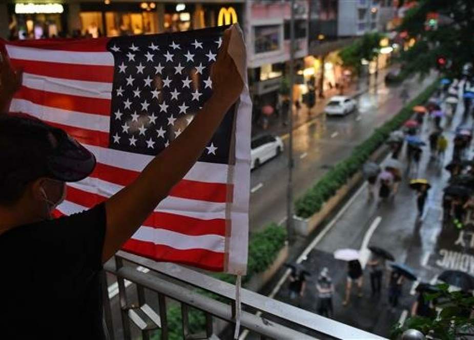 A man displays a US national flag as protesters walk along a street during a rally in Hong Kong.jpg