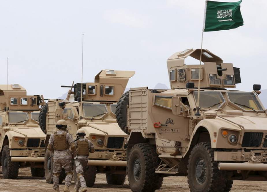 Saudi troops walk past armored personnel carriers at their base in Yemen