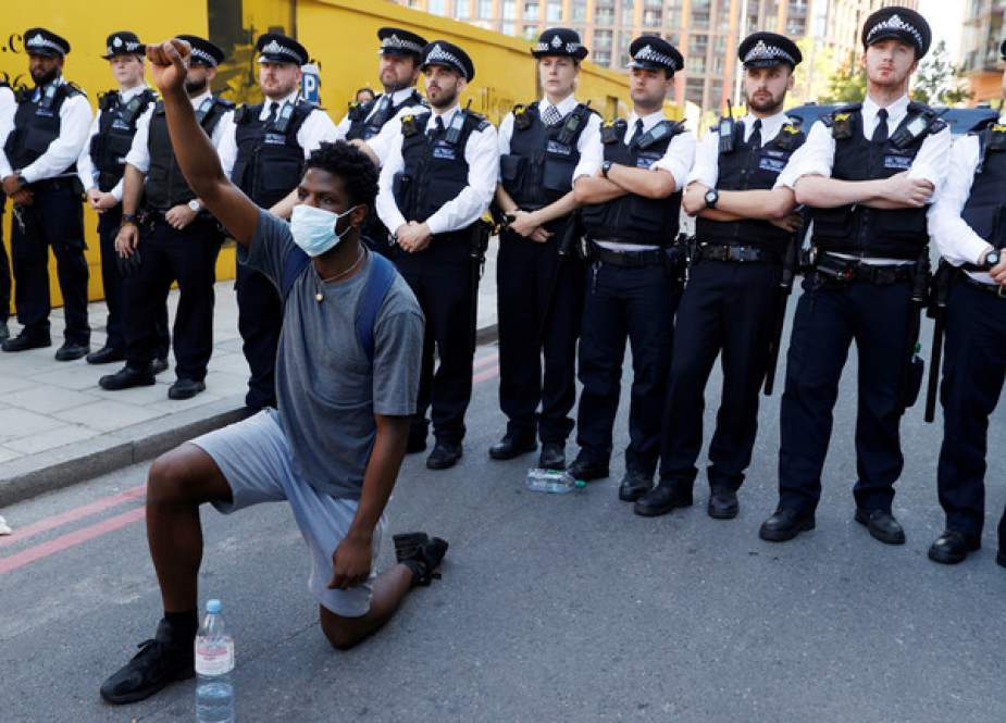 A man kneels in front of police officers during a protest near the US Embassy in London.JPG