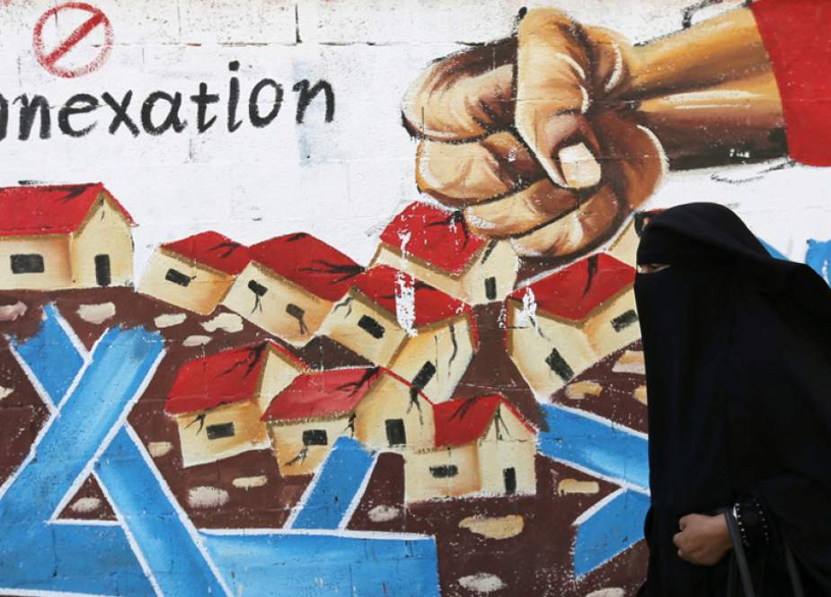 Palestinian woman walks past a mural in protest at Israel