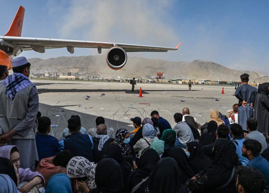 Afghan people sit as they wait to leave the Kabul airport in Kabul.jpg