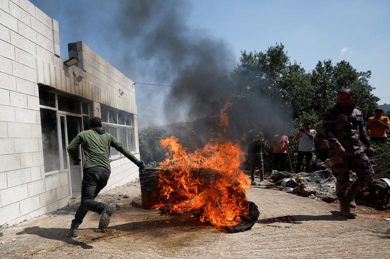 A Palestinian man runs near a burning object, after an attack by Israeli settlers, near Ramallah, in the Israeli-occupied West Bank, June 21, 2023.