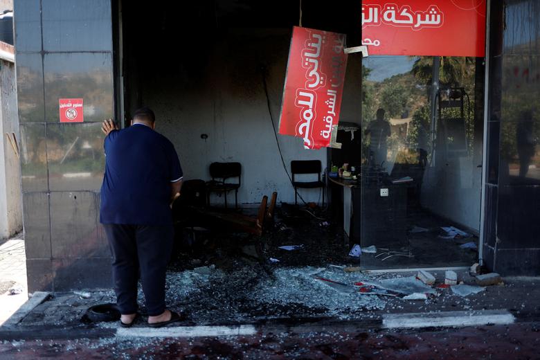 A Palestinian man clears broken glass at a store damaged in an attack by Israeli settlers near Ramallah in the Israeli-occupied West Bank, June 21, 2023.