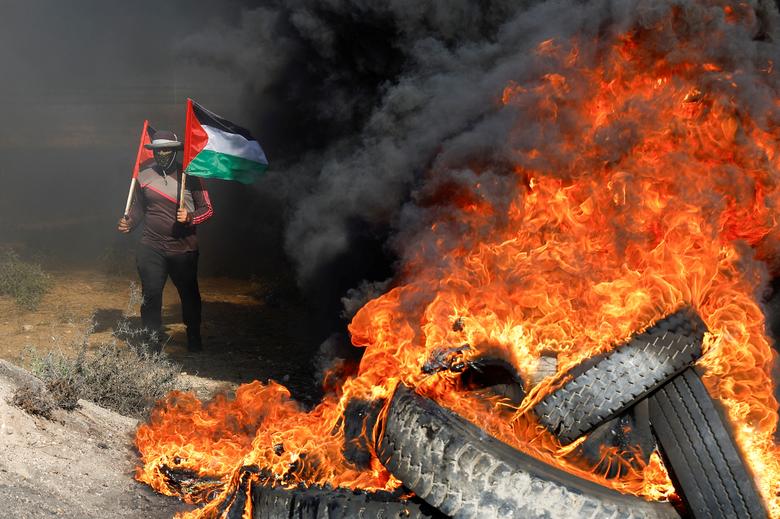 Seorang Palestina memegang bendera selama protes terhadap serangan tentara Israel di Jenin, di sepanjang pagar perbatasan Israel-Gaza di timur Kota Gaza 3 Juli