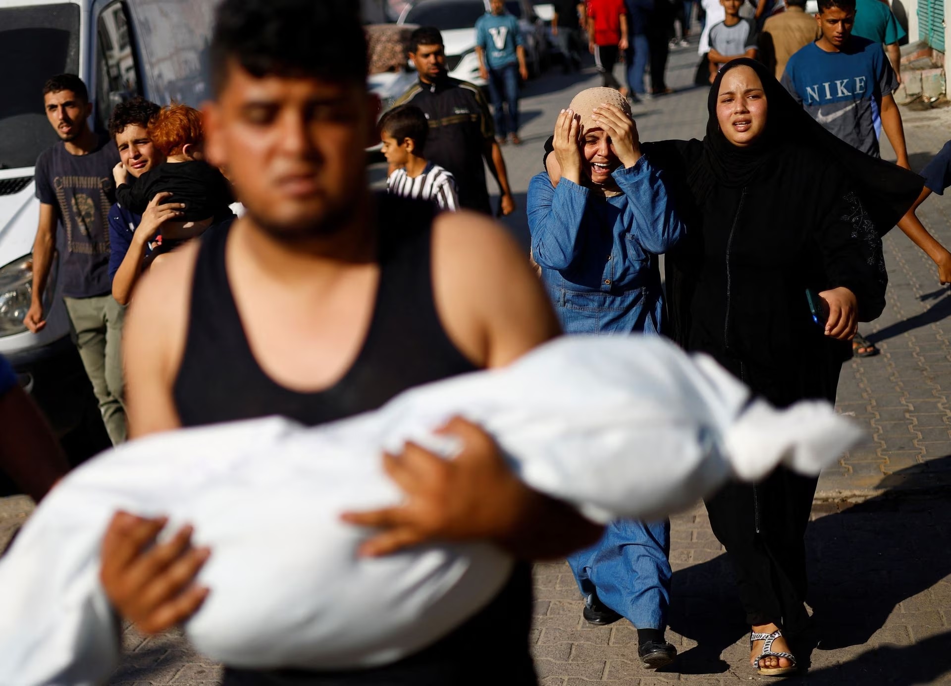 A man carries the body of a Palestinian child killed in Israeli strikes as mourners react, outside a hospital in Khan Younis in the southern Gaza Strip, October 17.