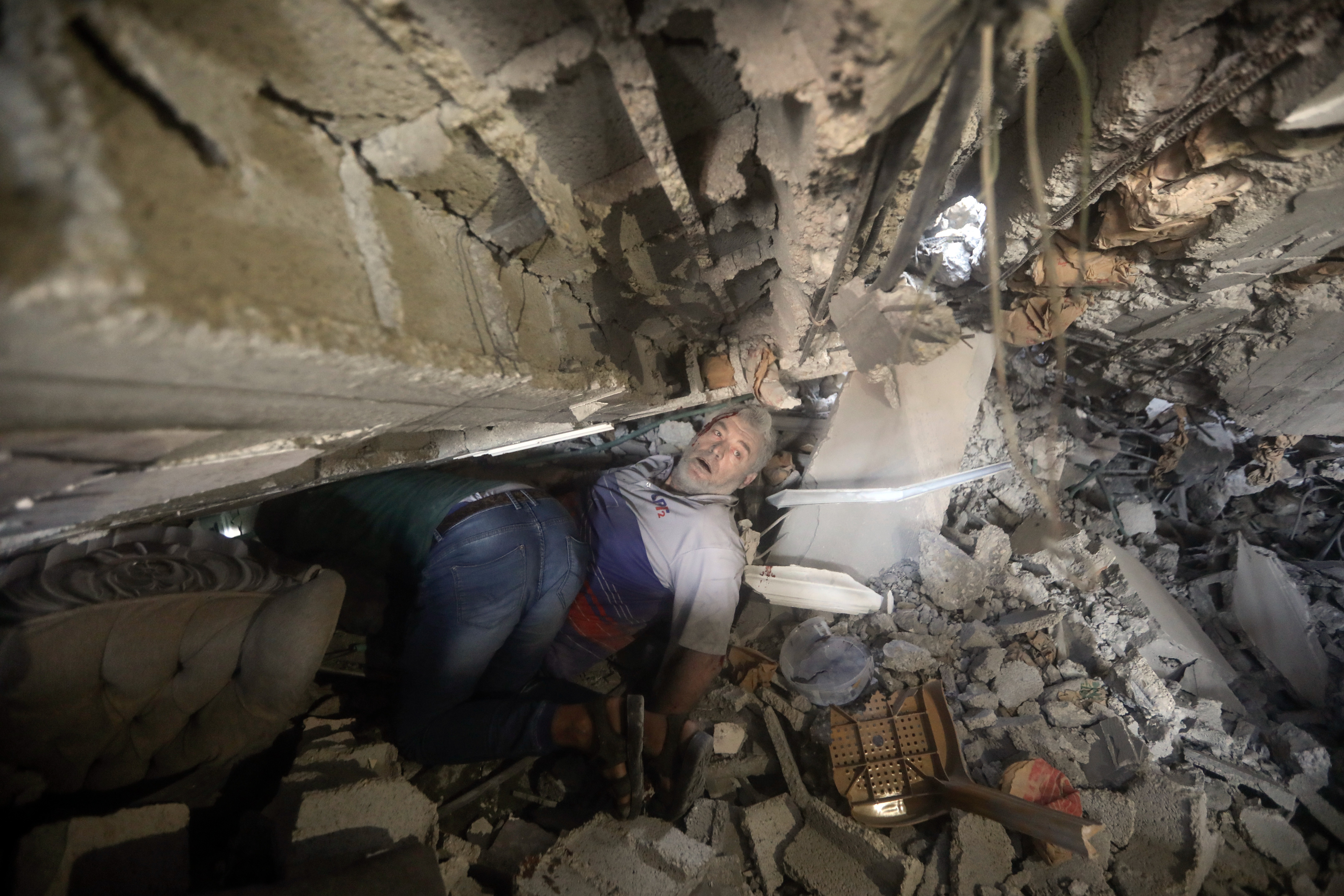 Orang-orang mencoba menyelamatkan seorang pria dari reruntuhan bangunan yang hancur akibat serangan udara Israel di kamp pengungsi Khan Younis
