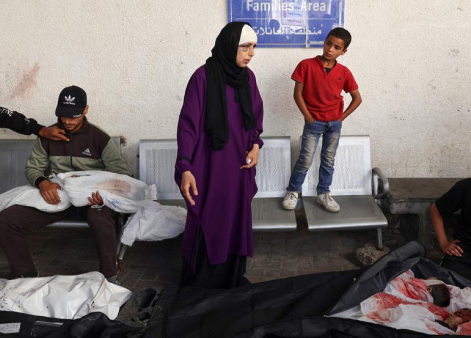 A Palestinian man holds the shrouded body of his child as a woman stands beside the bodies of her children, all killed in an Israeli bombing in Rafah